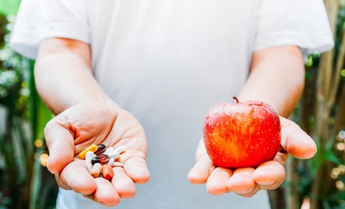 Person holds a red apple in one hand and a handful of pills in the other